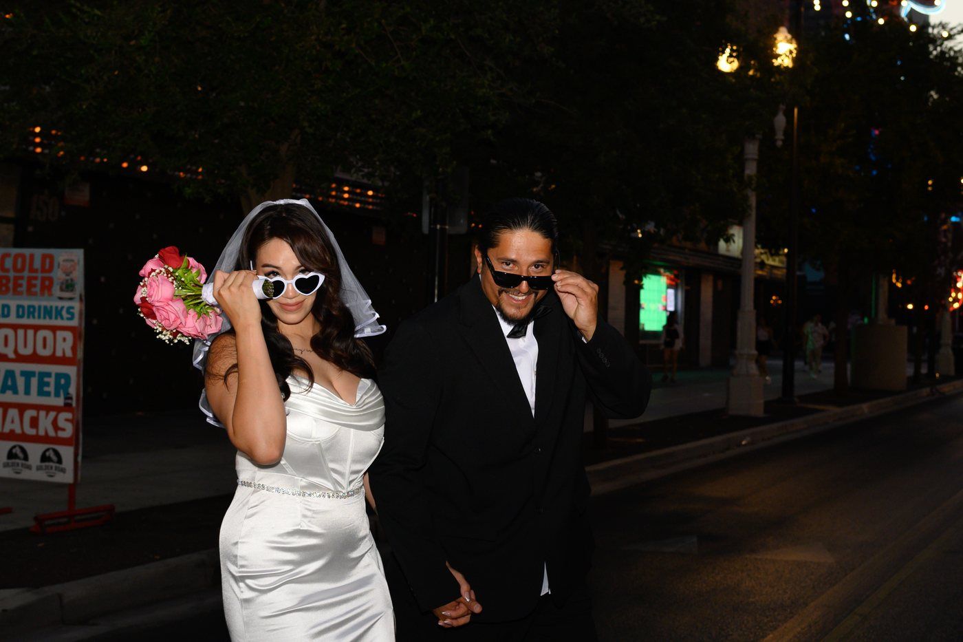 Playful newlyweds lowering their sunglasses on Fremont Street at night