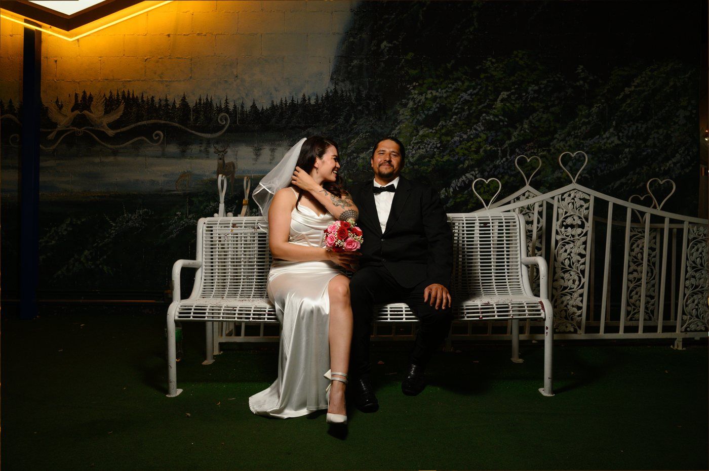 Bride and groom on a white heart-motif bench at the wedding chapel