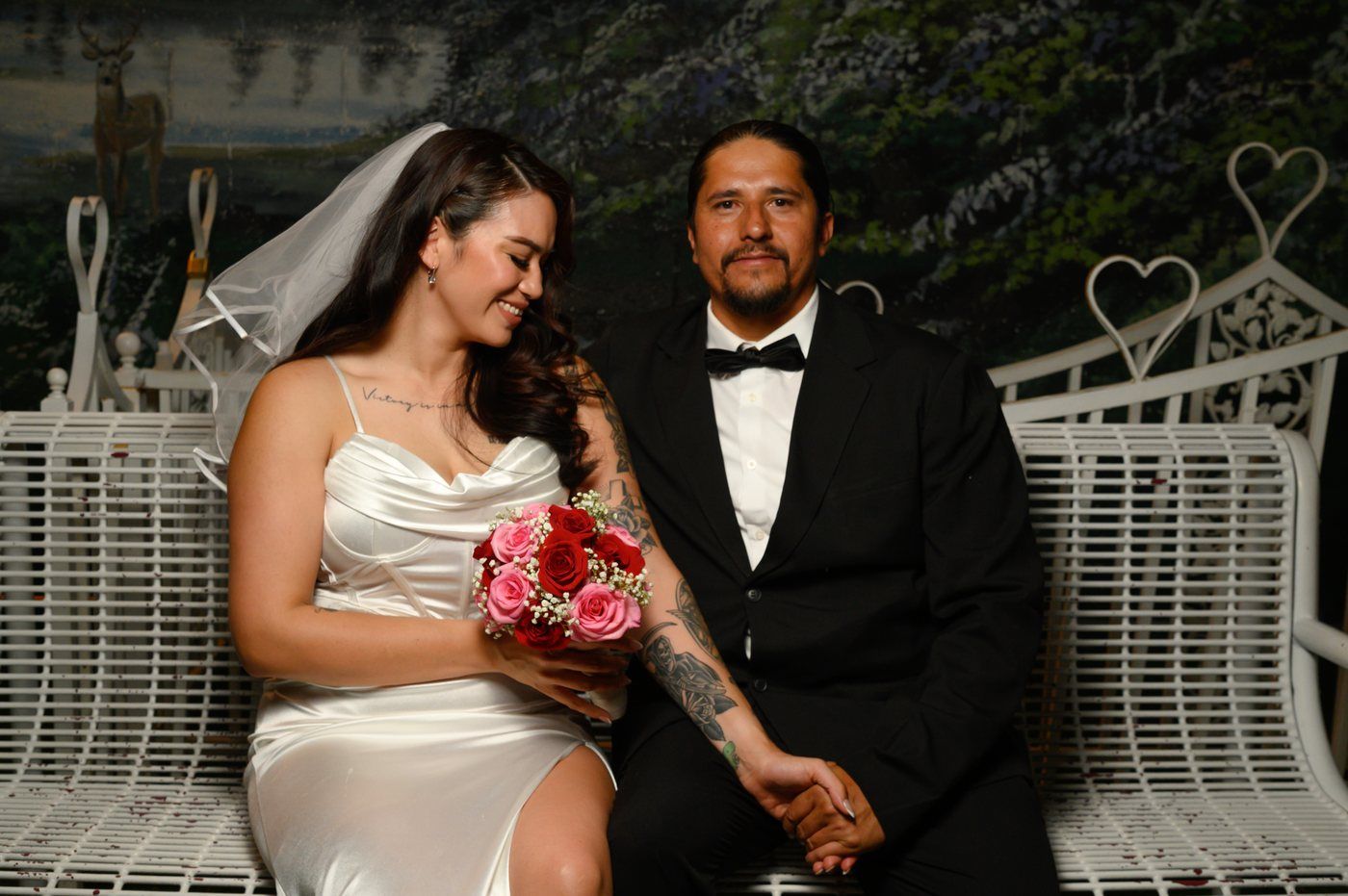 Bride and groom holding hands on the chapel bench with a rose bouquet