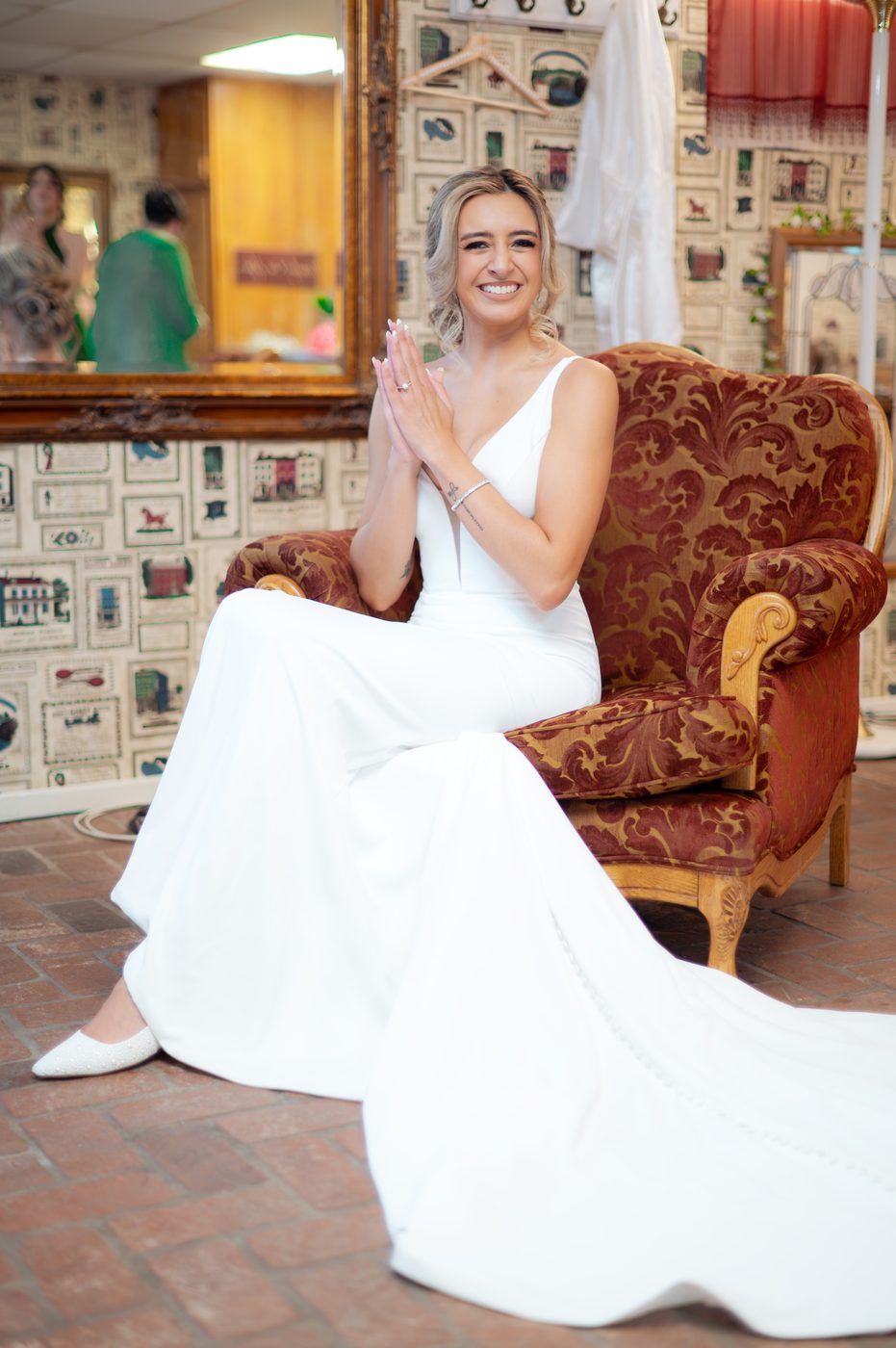 Bride seated in a vintage armchair, hands clasped, smiling